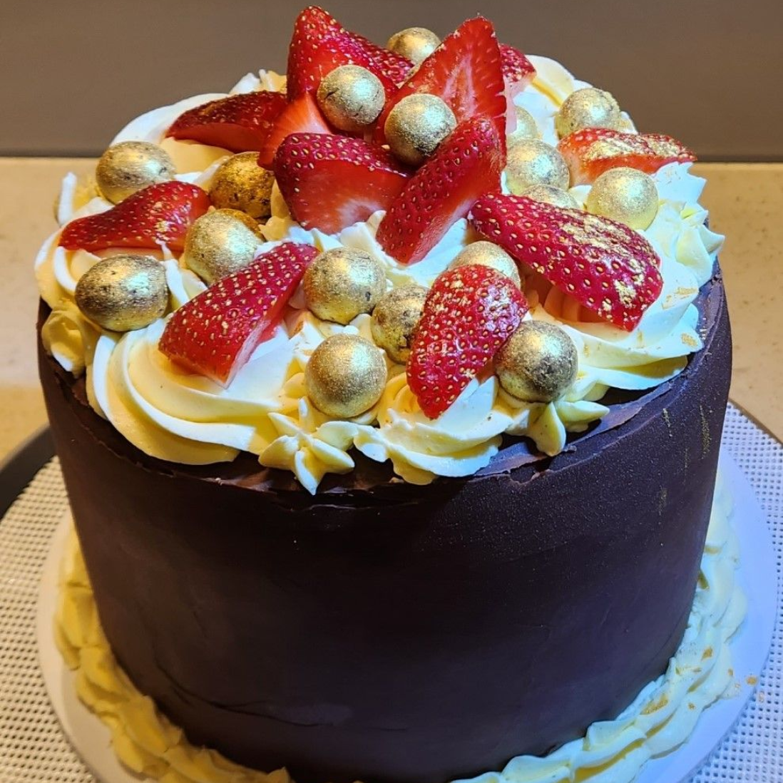 Chocolate cake with white frosting, sliced strawberries, and gold-covered chocolate balls.