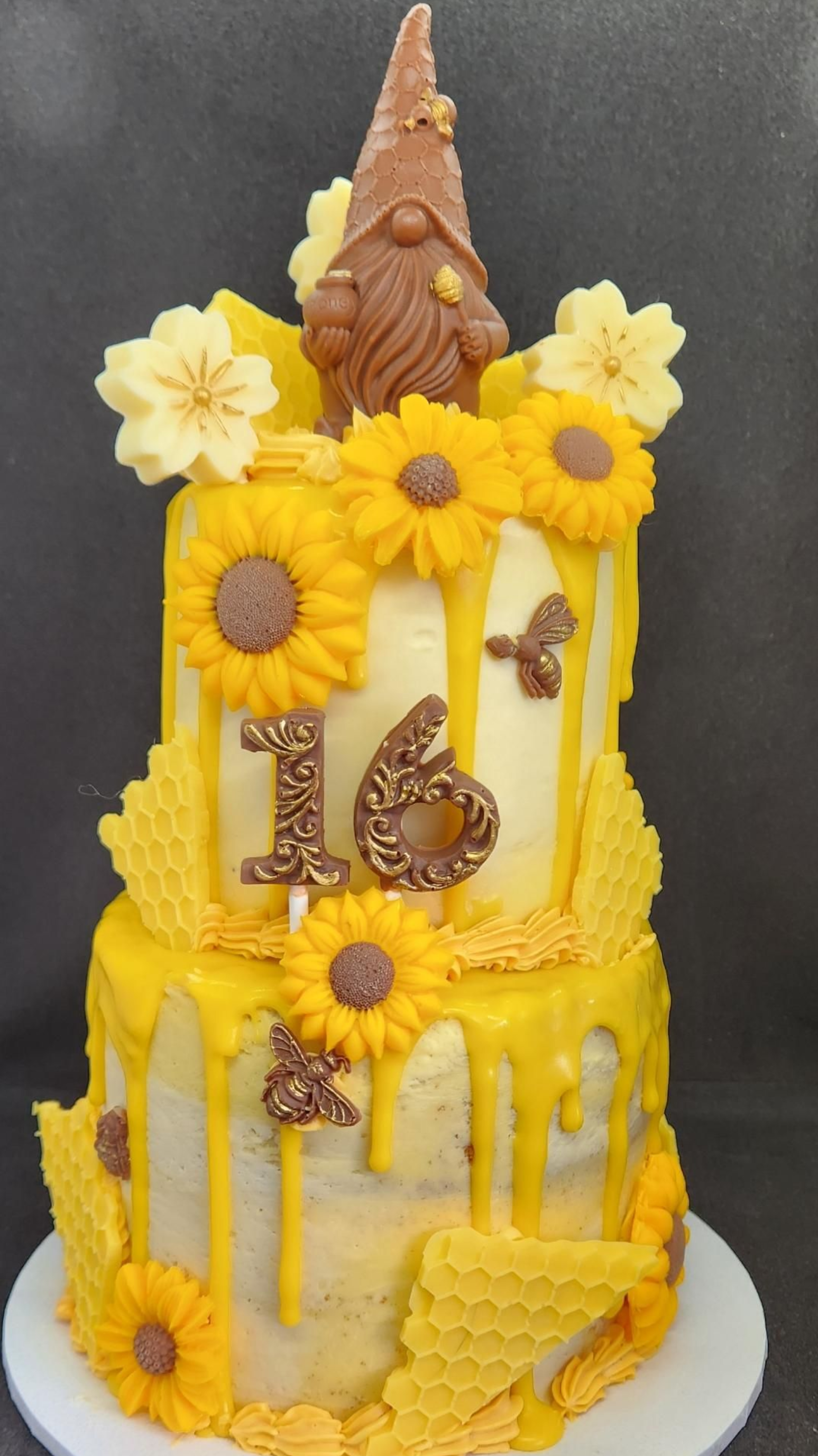 Two-tiered yellow cake decorated with sunflowers, chocolate gnome, and honeycomb for a 16th birthday.