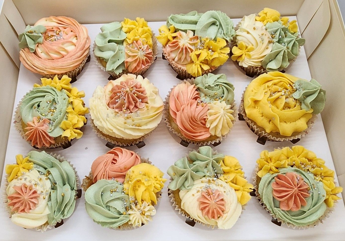 Box of 12 cupcakes with colorful, swirled frosting in shades of yellow, green, and peach.