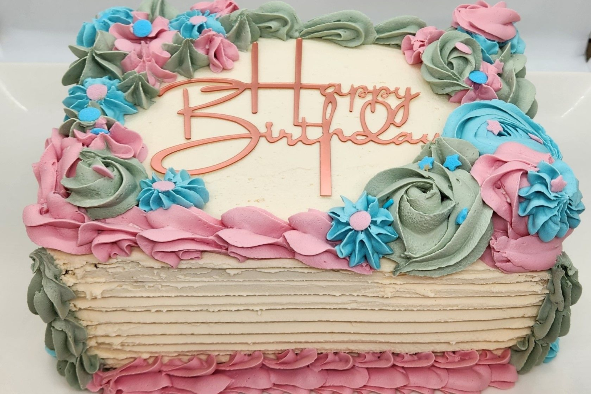 Square birthday cake with pink, blue, and green frosting flowers, 