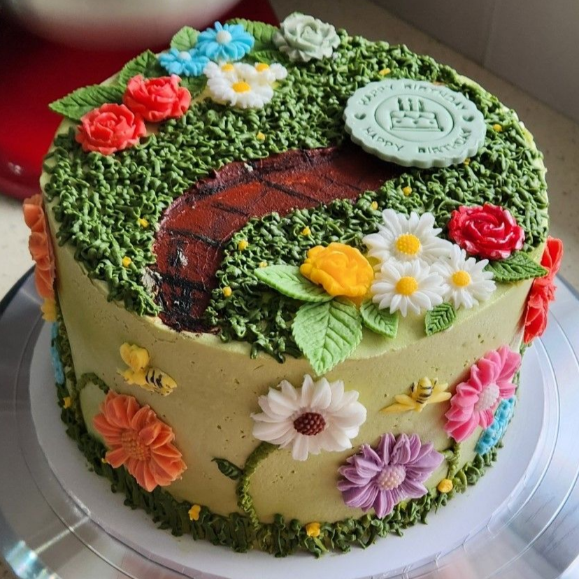 Garden-themed birthday cake with green frosting, a brick pathway, and colorful flower decorations.