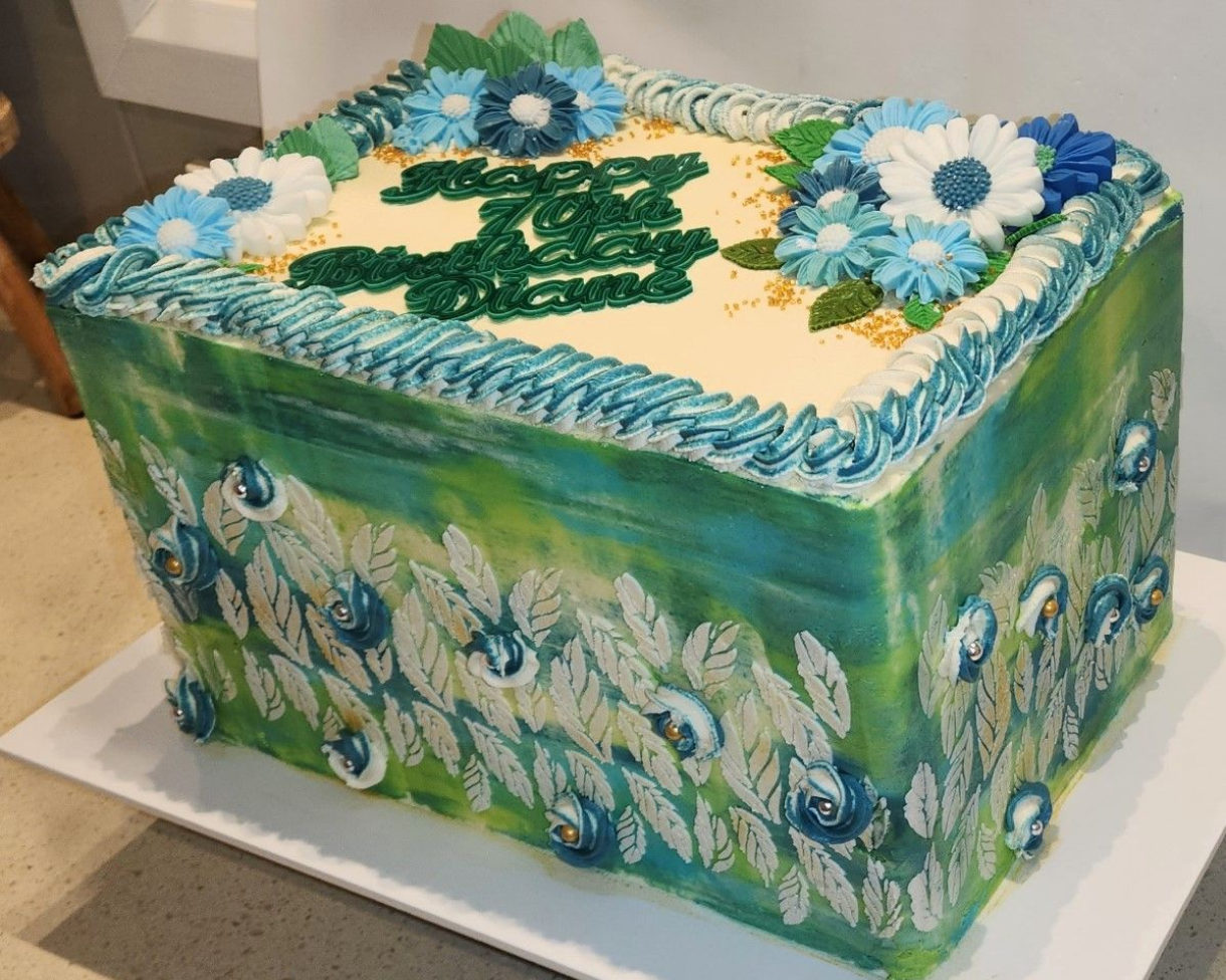 Cake decorated with peacock feather design in teal, green, and blue, with floral accents and 