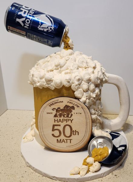 Beer mug cake with overflowing foam, tilted can, and 50th birthday message.