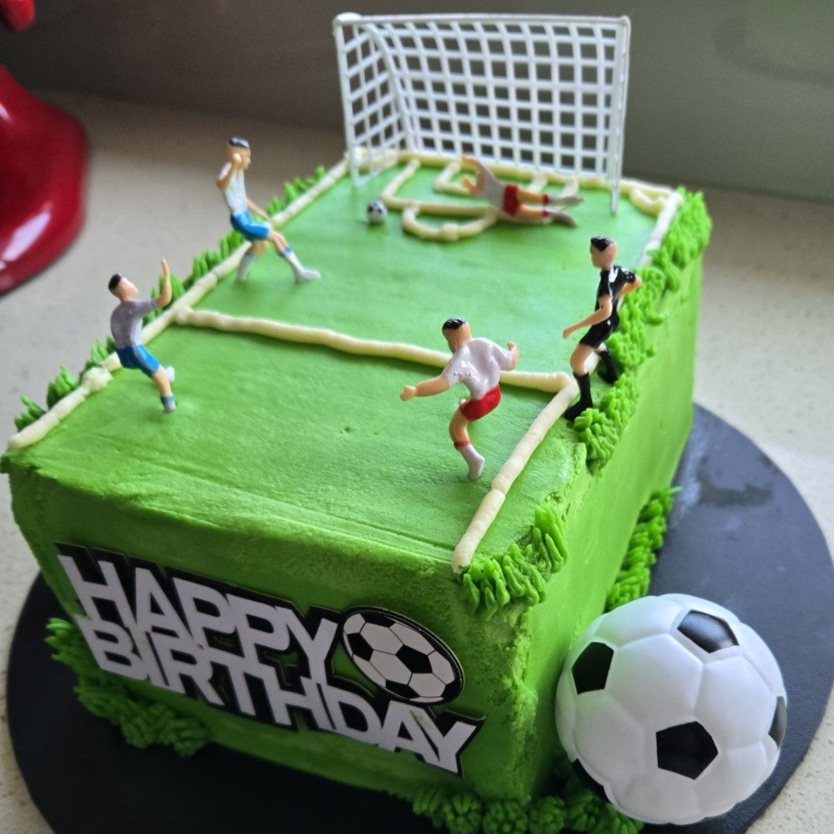 Soccer-themed birthday cake with green frosting, miniature players, goal, and soccer ball; 