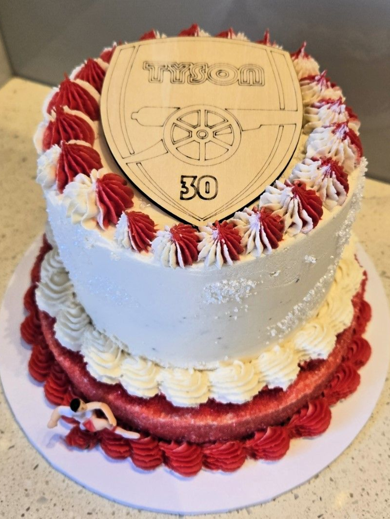 Two-tiered birthday cake with Arsenal crest, red and white frosting, and 