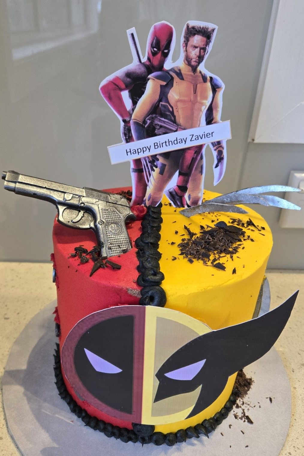 Deadpool and Wolverine birthday cake with logos, gun, and claws. Red and yellow frosting, 