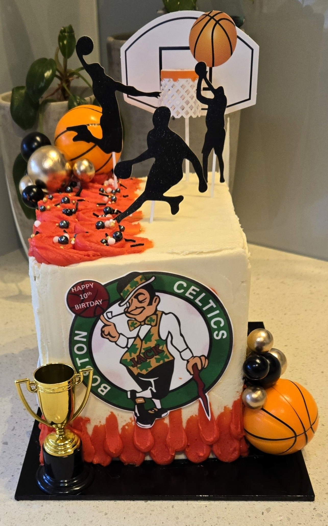 Basketball-themed cake with Celtics logo, basketball player silhouettes, and decorative balls.