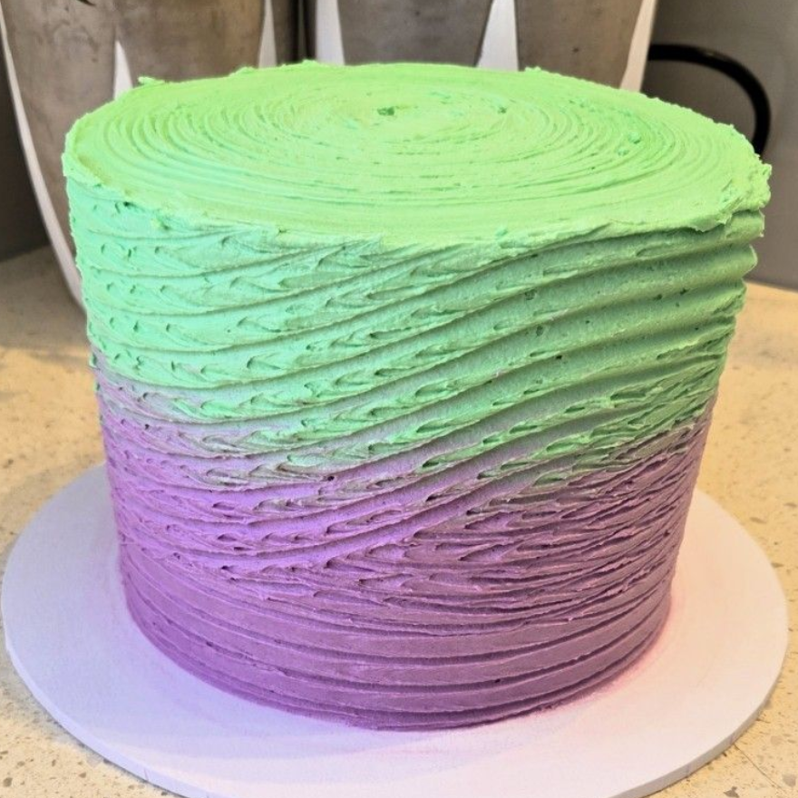 Cake with green and purple ombre frosting, textured vertical and spiral design.