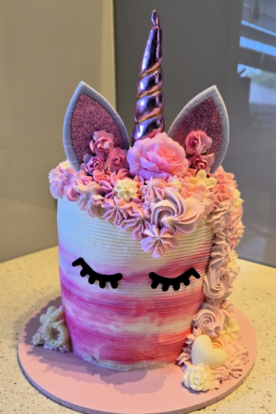 Unicorn cake with pink and white frosting, sparkly ears, a metallic horn, and closed eyes.
