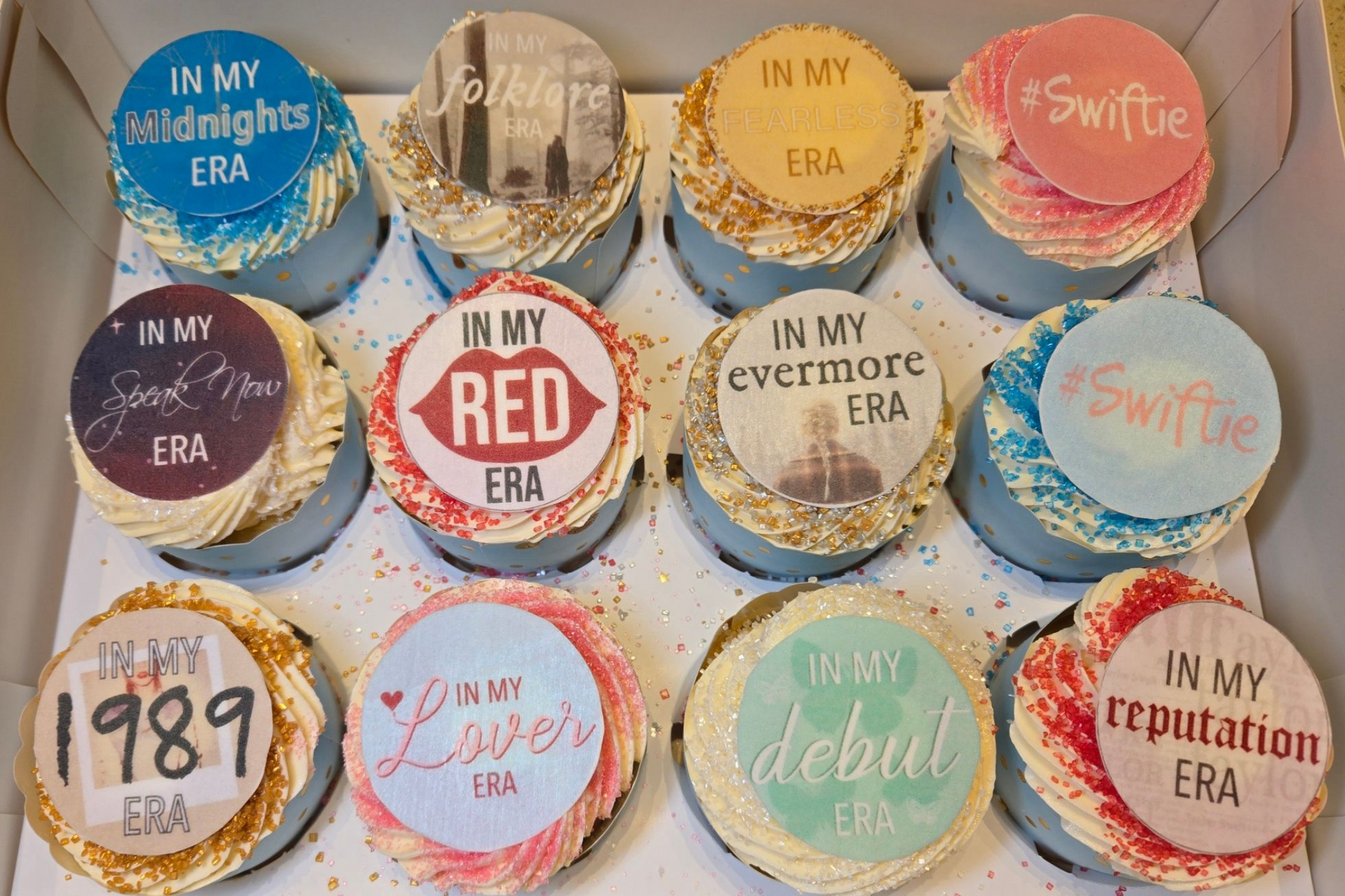 Box of cupcakes decorated with Taylor Swift album themes.