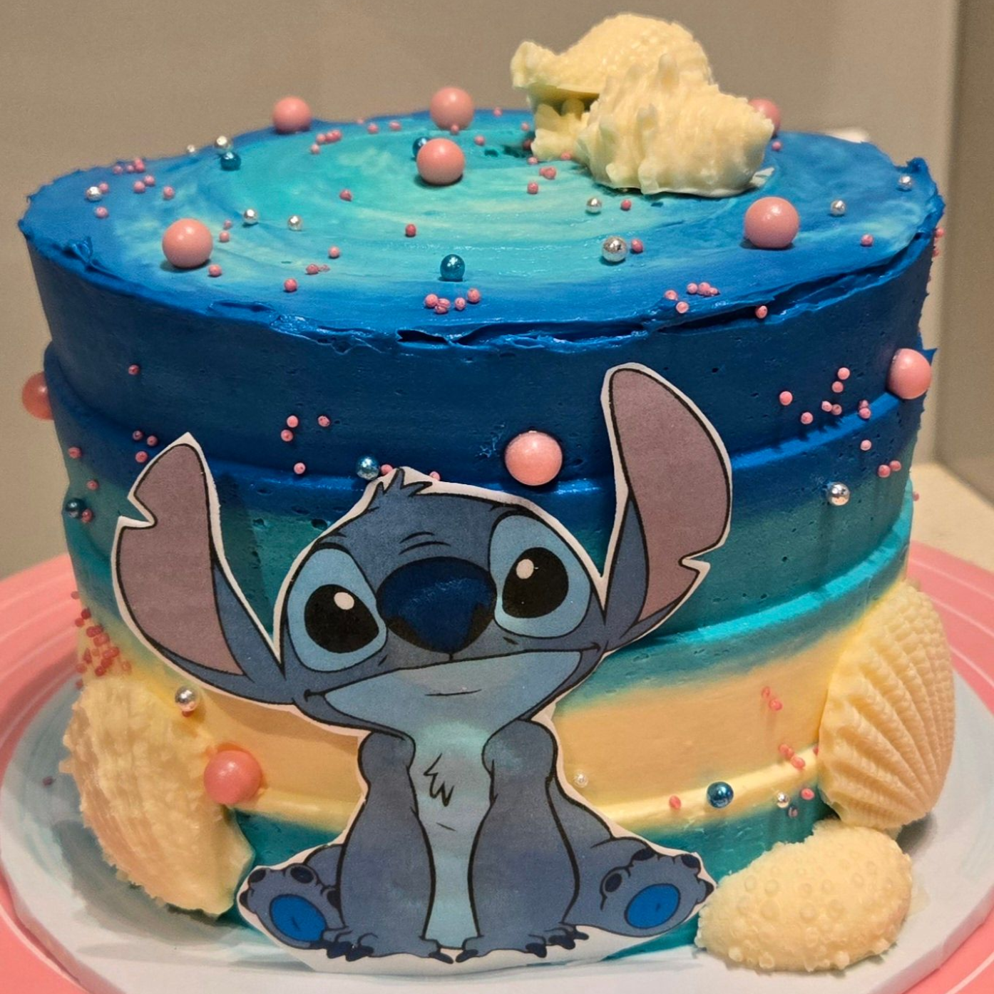 Cake decorated with a Stitch character, ocean-themed frosting, and edible seashells.