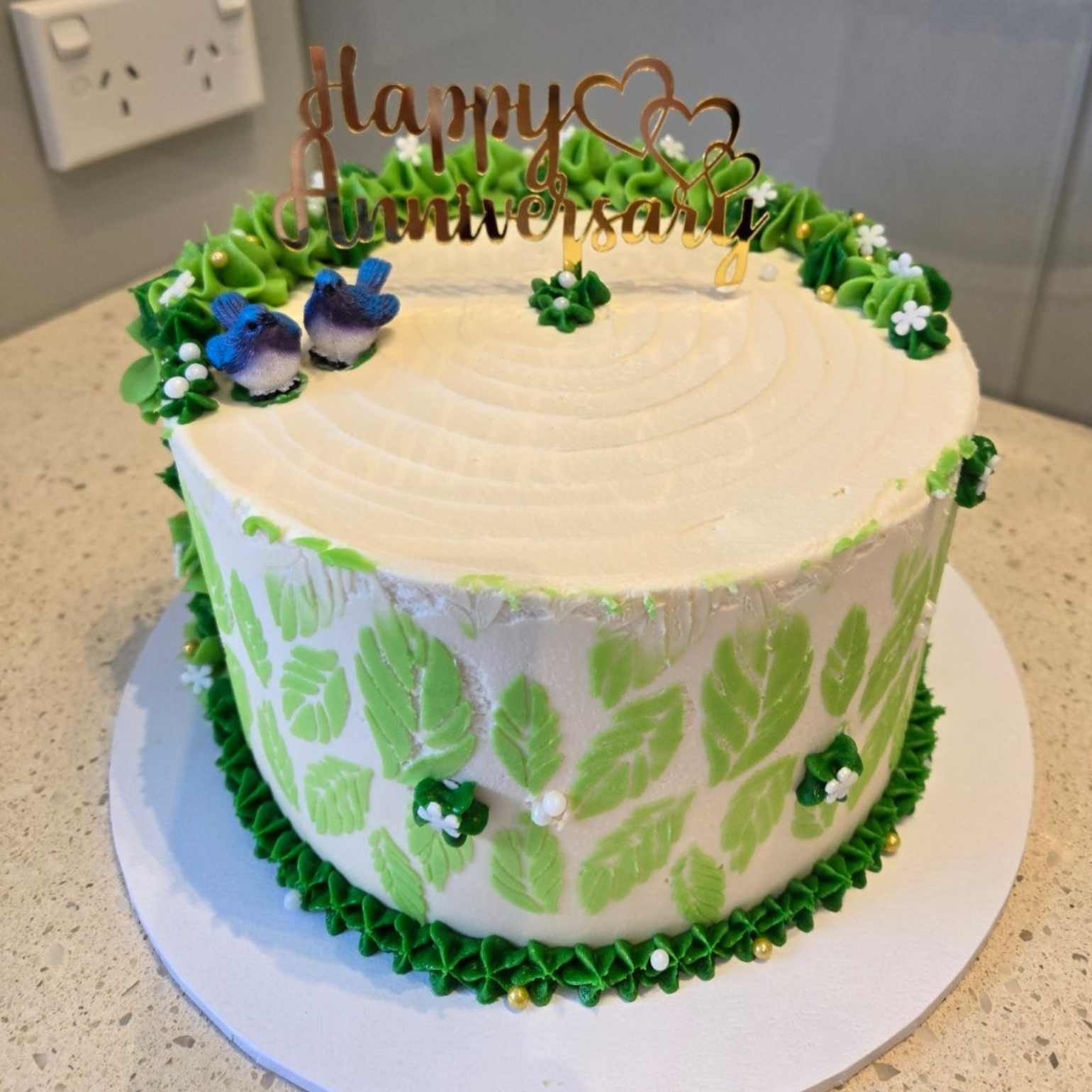 Anniversary cake with green leaf design, two blue birds, and gold 