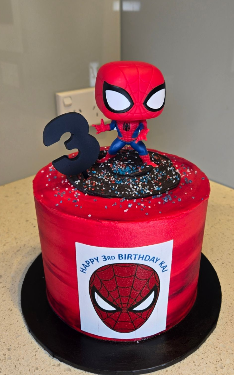 Red Spiderman-themed birthday cake with a Spiderman figure on top, black 