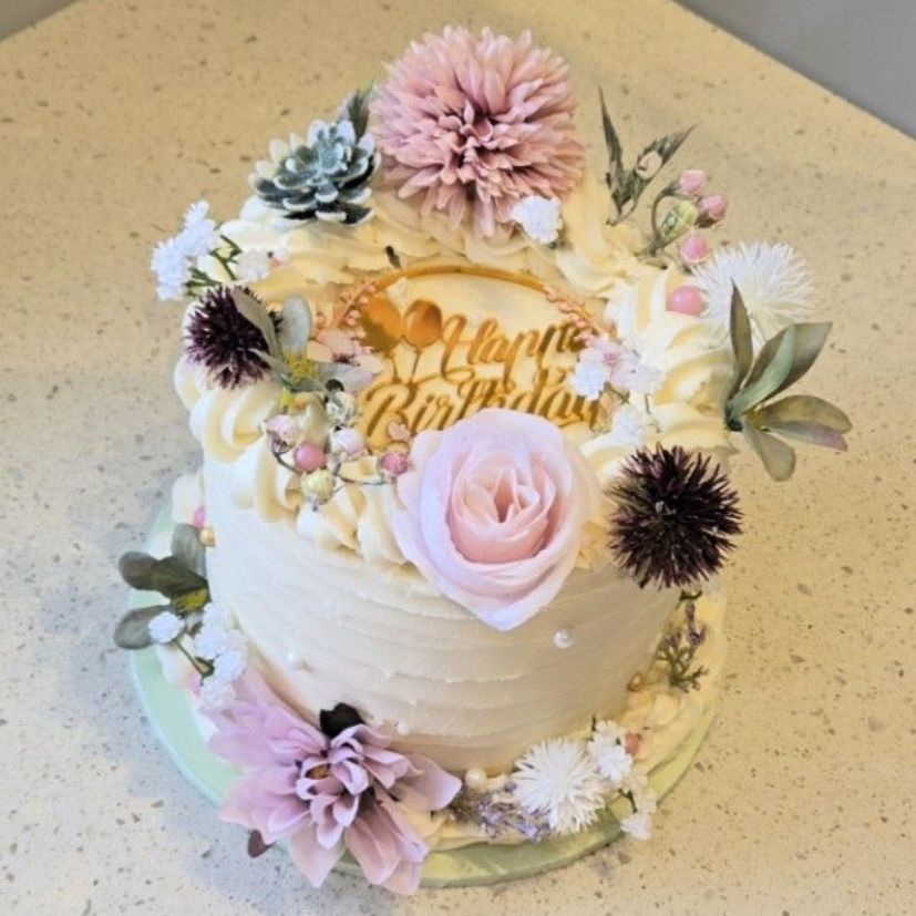 Birthday cake decorated with frosting and pastel flowers, a gold 