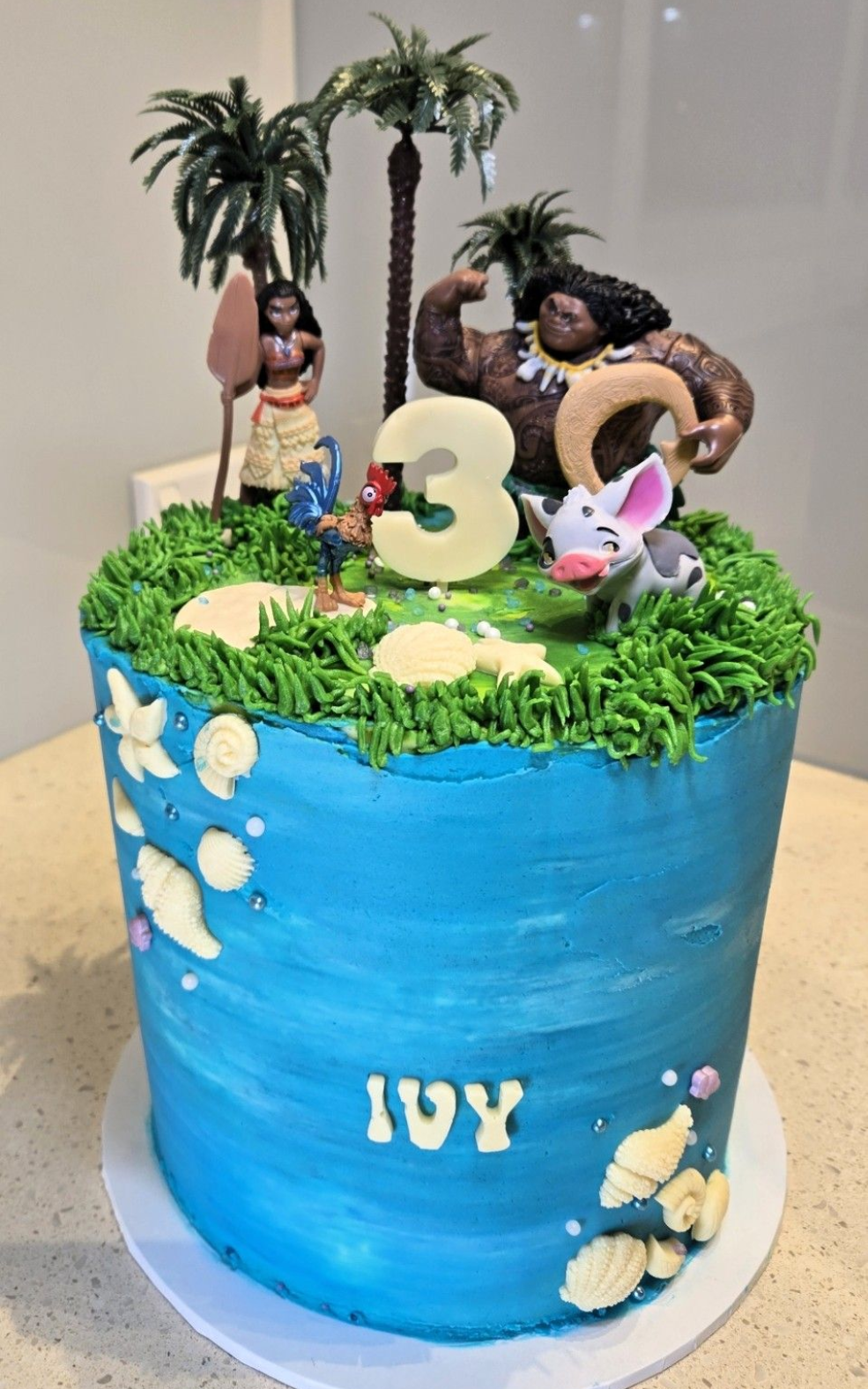 Moana-themed birthday cake with figures, grass, blue frosting, and 