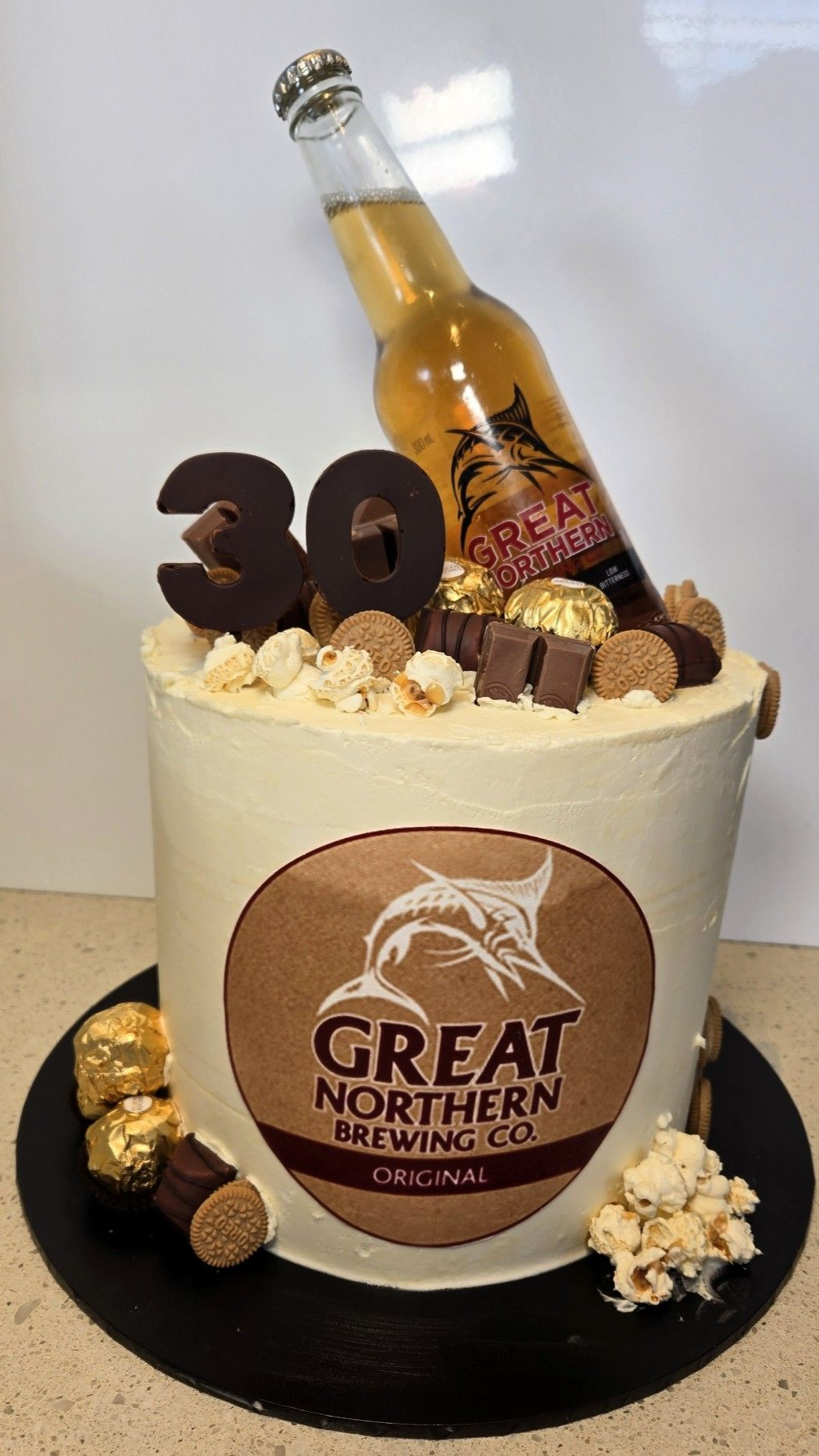 Cake decorated with beer bottle, logo, 30, chocolates, and popcorn.