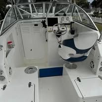 Boat cockpit with white seats and steering wheel, viewed from the rear deck.