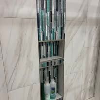 Narrow bathroom shelf with rows of toiletries and bottles against beige marble tile.