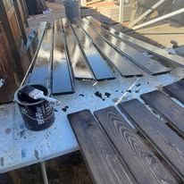 Metal deck boards and a paint bucket on a rooftop under construction, with one board partially installed.
