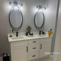 Modern bathroom vanity with two oval mirrors, white cabinets, black fixtures, and small decor items.