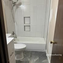 Small bathroom with white tub, tiled shower wall, vanity, and gray floor.