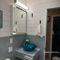 Small bathroom vanity with silver mirror, white shiplap walls, gray tile, and blue decorative bowls.