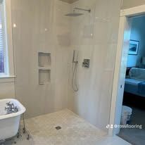 White tiled walk-in shower with recessed shelves, grab bars, and handheld showerhead beside a bedroom doorway