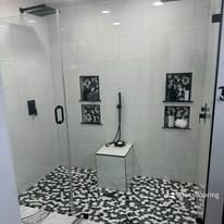 Modern glass shower stall with black-and-white mosaic floor and wall niches holding toiletries