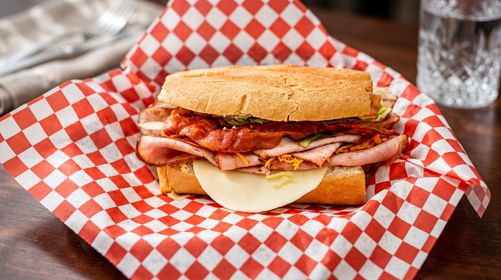 Sandwich with bacon, egg, and melted cheese on red checkered paper