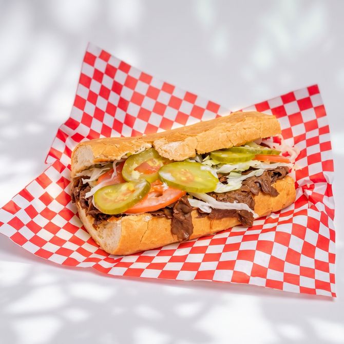 Sandwich with scrambled eggs and meat in red-and-white checkered wrapping paper on a dark table