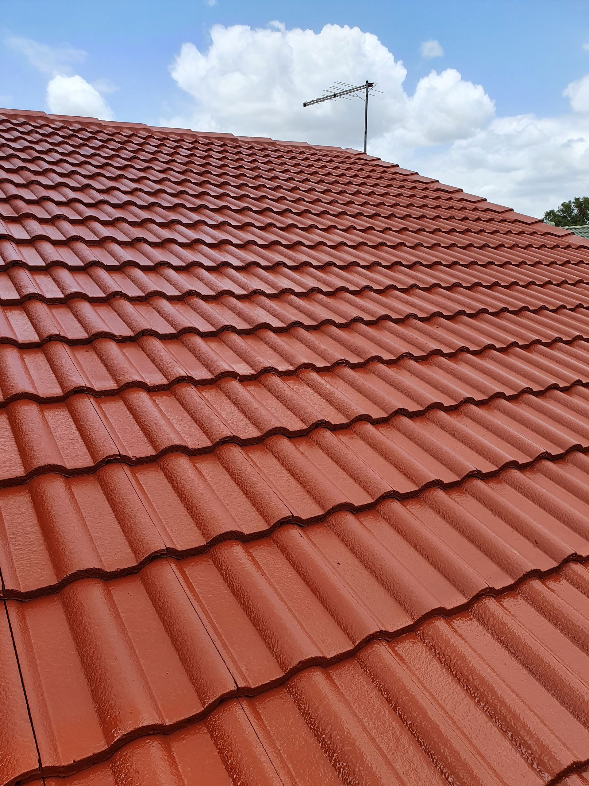 Red Tile Roof Under a Cloudy Blue Sky, With a Rooftop Antenna Visible — Keppel Coatings in Pacific Heights, QLD