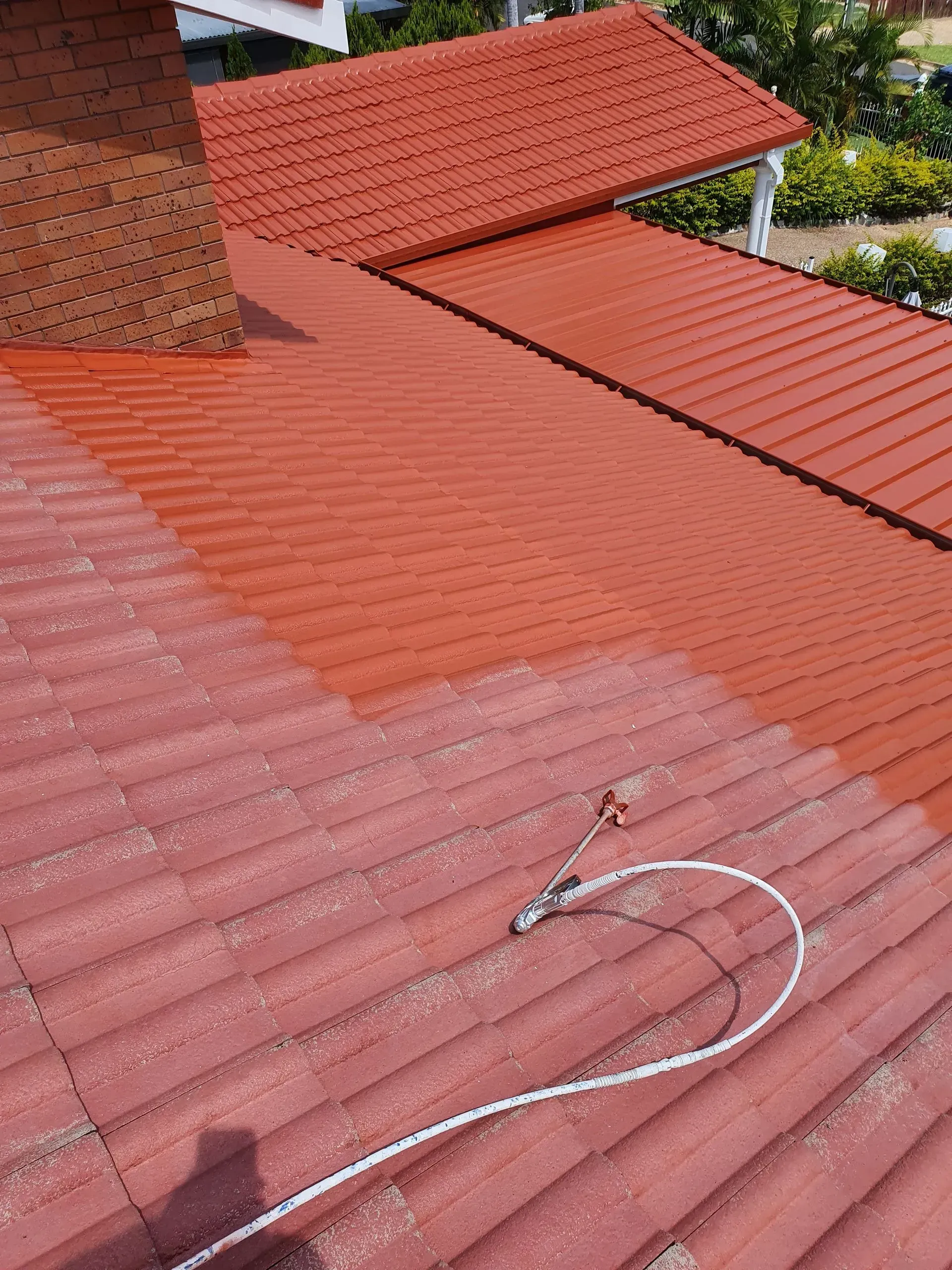 Red Corrugated Roof Being Repainted With a Spray Gun — Keppel Coatings in Pacific Heights, QLD