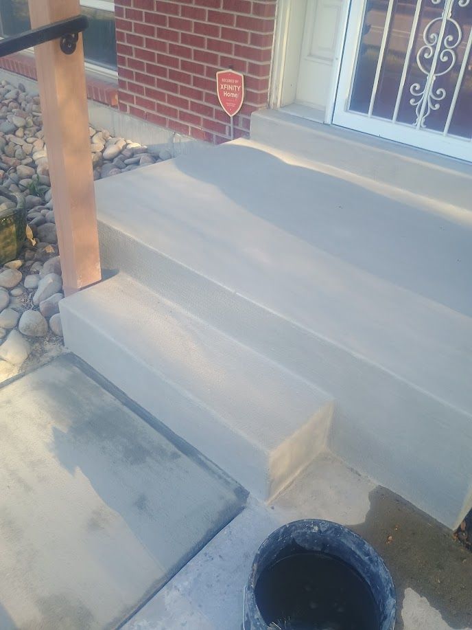 Concrete front steps with a brick wall, wooden post, and an open drain nearby