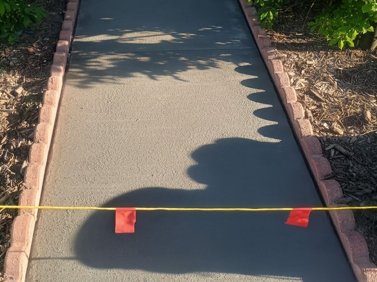 Outdoor walkway blocked by a yellow rope and small red markers, with tree shadows across the path