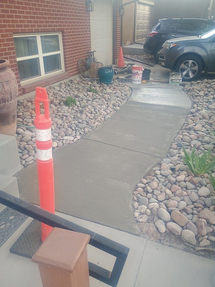 Front walkway under repair beside a brick house, with gravel, orange cone, and parked car nearby.