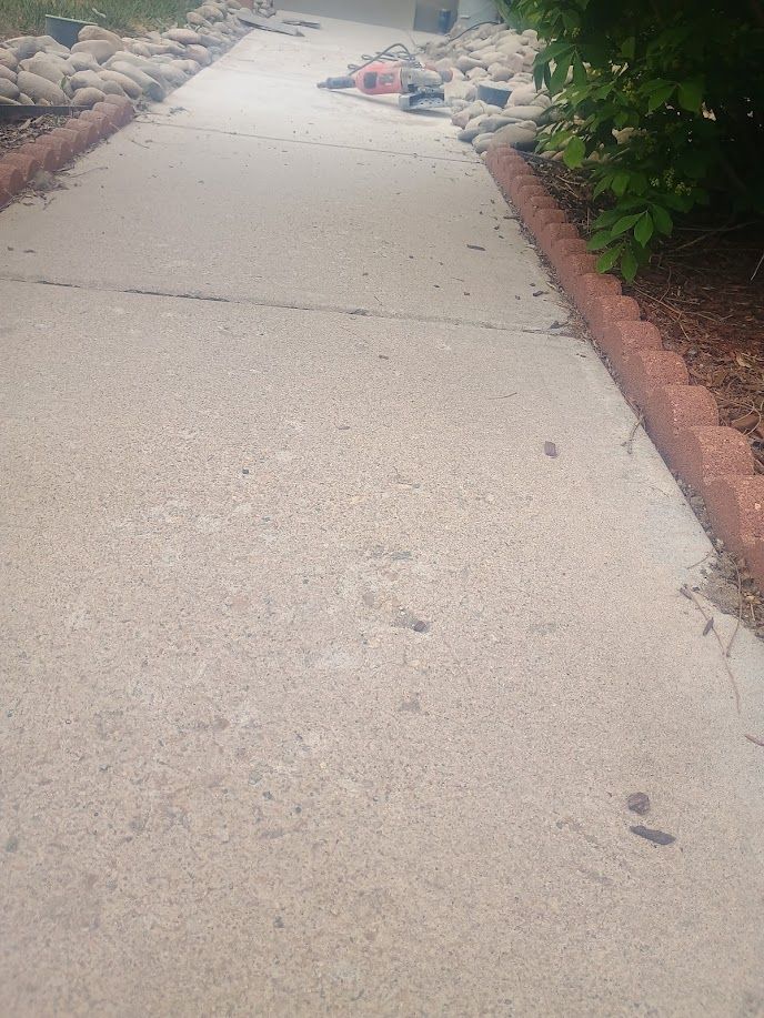 Concrete sidewalk with a raised, cracked section beside red edging and greenery