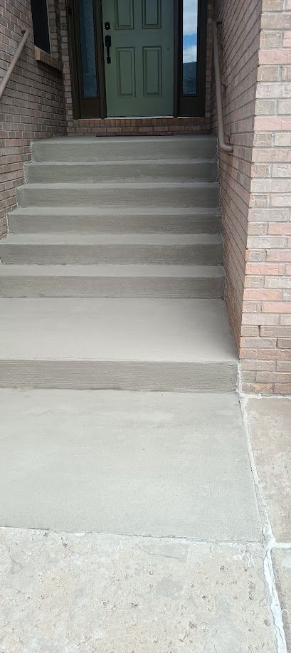 Concrete front steps leading to a dark green front door and brick entryway