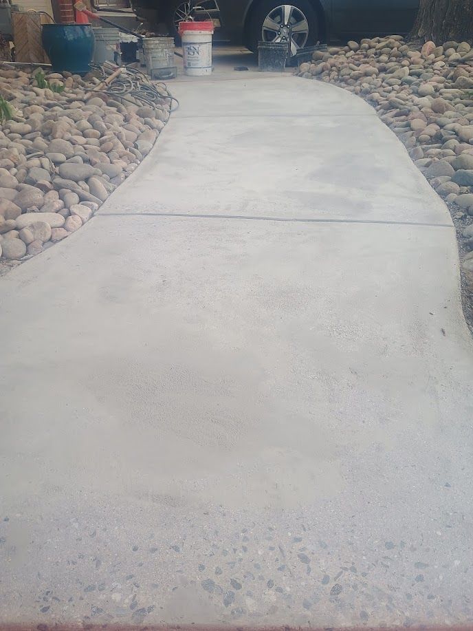 Concrete walkway bordered by river rocks and potted plants, leading into a yard