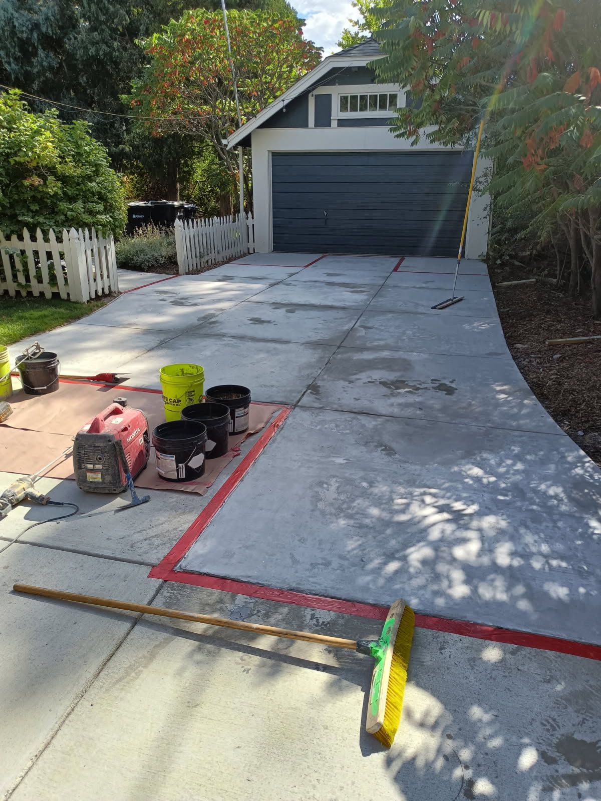 Concrete driveway under construction with red guide lines, tools, and a garage at the end.