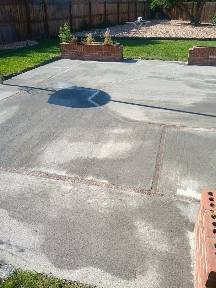 Wet concrete driveway with a dark puddle and small brick planters near a wooden fence