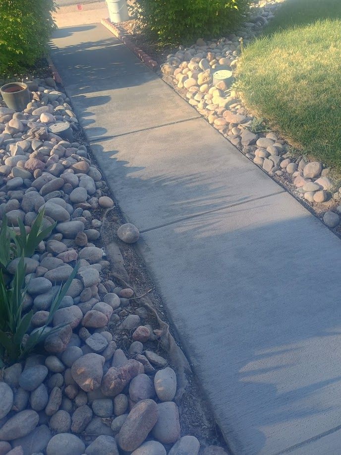 Concrete sidewalk between landscaped rock beds beside green grass in warm sunlight