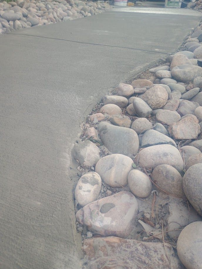 Curved concrete walkway beside a bed of smooth river rocks outdoors