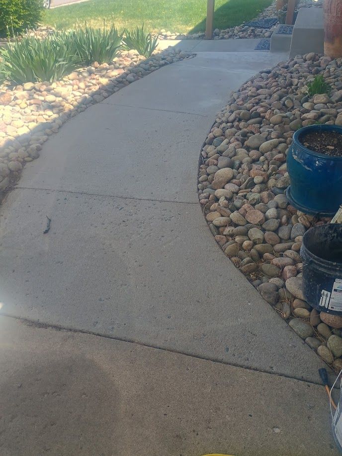 Curved concrete walkway beside a rock garden and potted plants in a sunny yard
