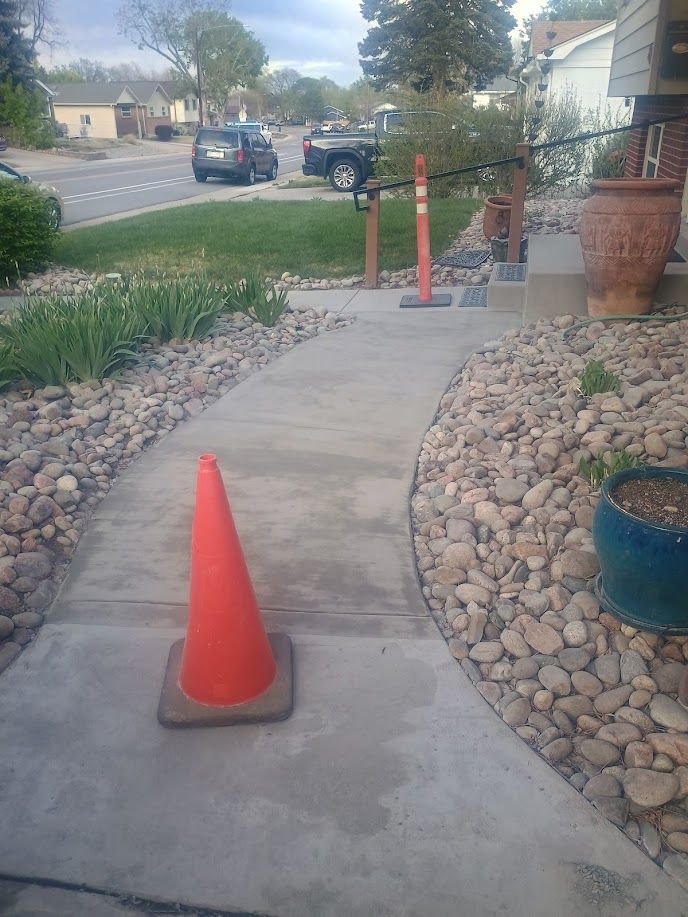Concrete walkway with orange cones blocking a path in a suburban yard near parked vehicles