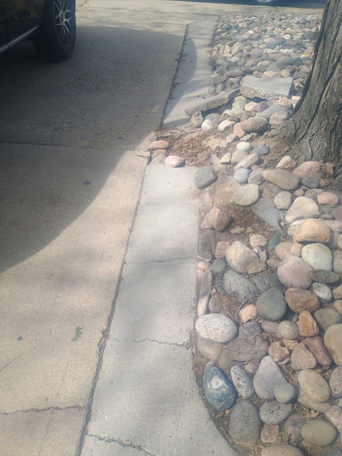 Sidewalk beside a street and tree bed filled with smooth rocks and snow