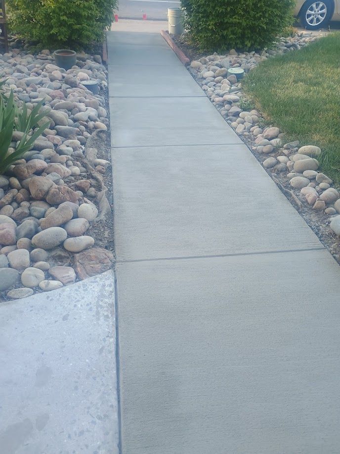 Concrete sidewalk path bordered by decorative rocks and grass, leading toward a driveway and parked car.