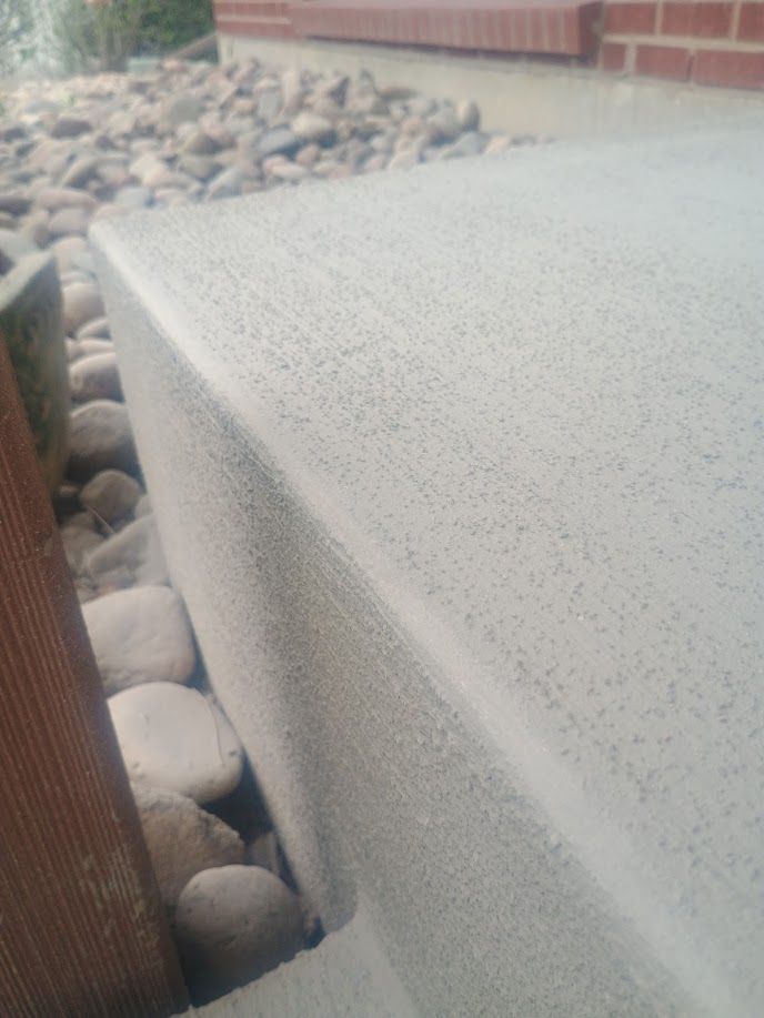 Close-up of a light gray stone step beside river rocks and a wooden fence outdoors