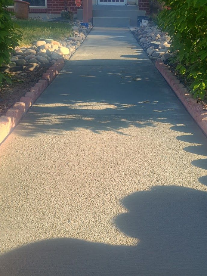 Sunlit concrete walkway lined with flower beds leading to a house entrance
