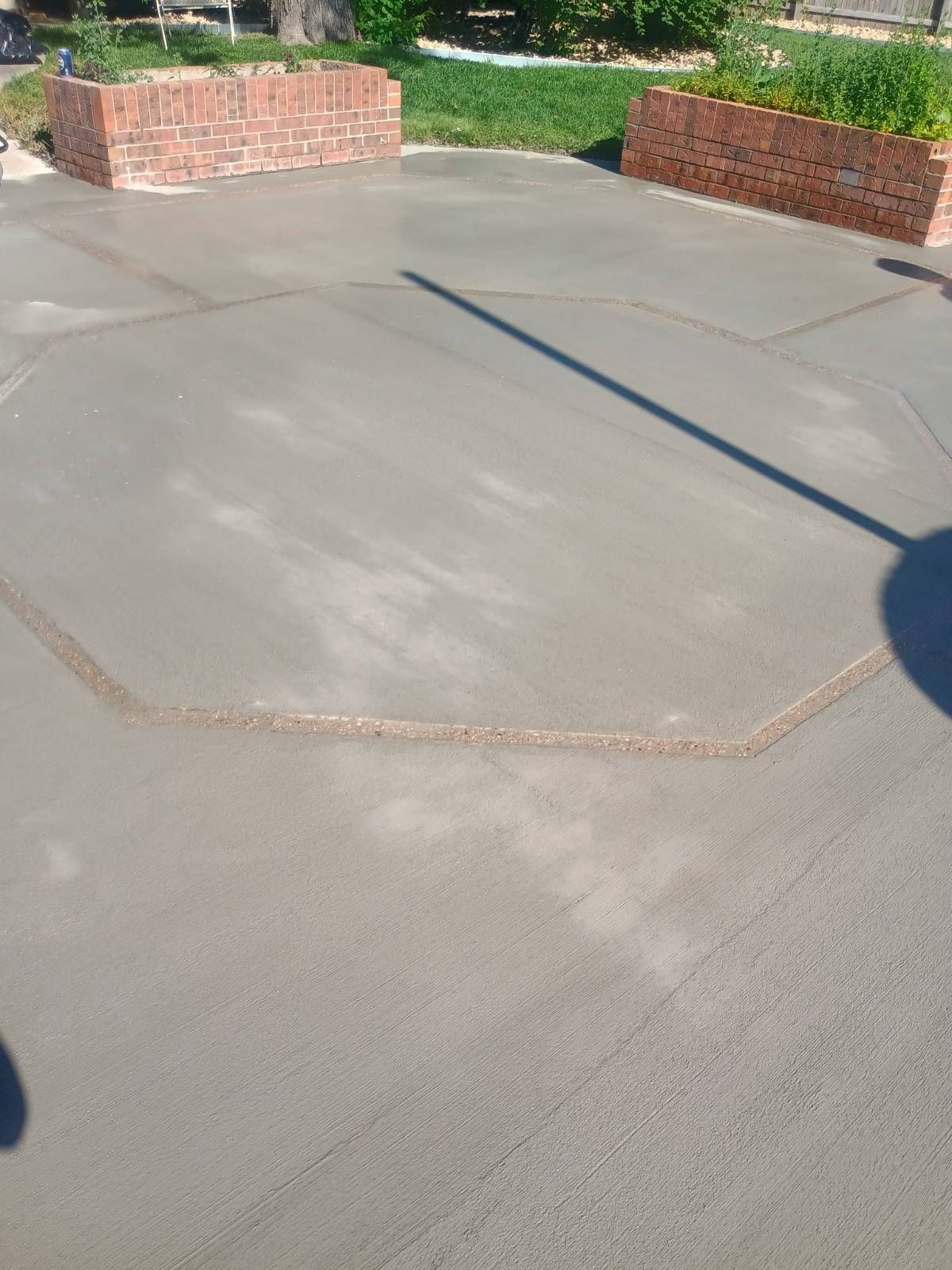 Concrete patio with a hexagonal outline, brick planters, and a long shadow in bright sunlight