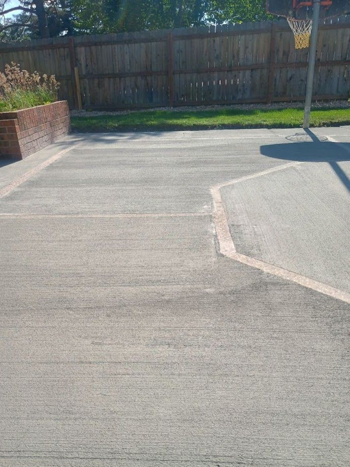 Empty concrete driveway beside a wooden fence and brick planter in bright sunlight